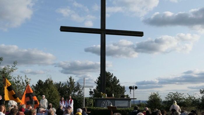 Eine große Menschenmenge versammelt sich vor einem hohen Kreuz unter einem bewölkten Himmel.