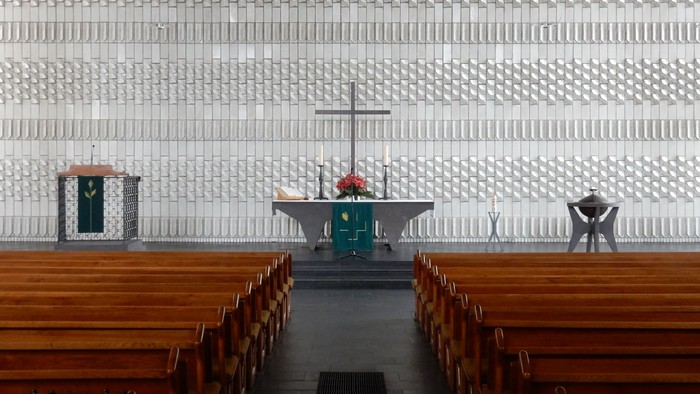 Leere Kirche mit Holzgestühl und Altarraum mit Kreuz und Kerzen