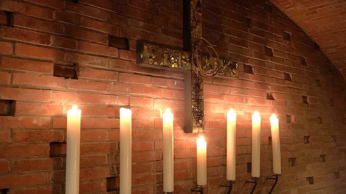 Brennende Kerzen vor einem Kreuz an einer Ziegelwand