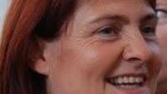 En smilende kvinde med kort rødt hår iført en lys top og halskæde.