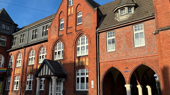 Historisches Backsteingebäude mit Bogenfenstern und dekorativer Steinverzierung, das eine kleine Eingangshalle aufweist.