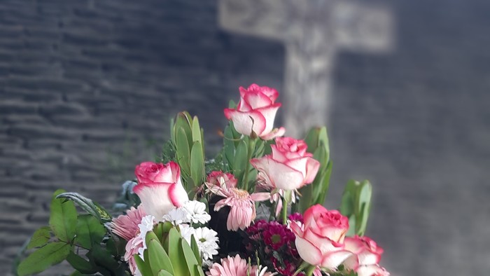 Blumenstrauß in Vase vor Kreuz an der Wand