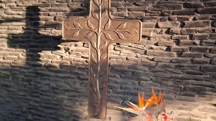 Kreuz an der Wand mit Blumen vorn.