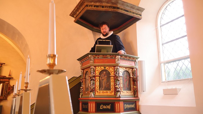Mand i prædikestol i kirke, glasmosaikvindue.