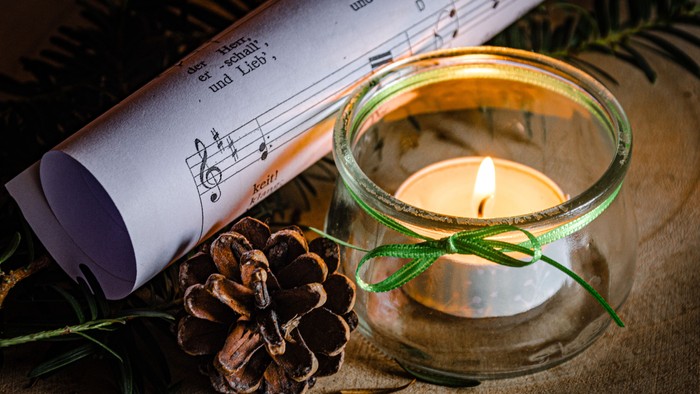 Kerze im Glas mit Band, Tannenzapfen und Notenblattrolle