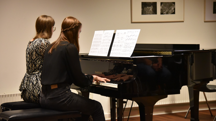 To kvinder øver klavermusik sammen med noderne åbne på klaverbænken.
