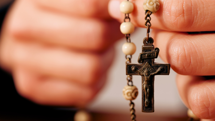 Eine Person hält ein Rosenkranz mit Kreuz.