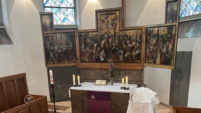 Altarraum einer Kirche mit Hochaltar, auf dem Boden liegen ein Kelch und ein Brot, beides gefertigt aus Holz.