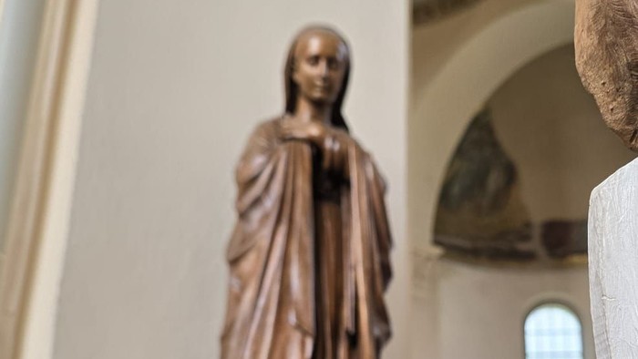Die Statue eines Kindes mit großen Kopf steht vor einer Jesus-Statue in einer Kirche.