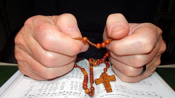 Hände halten Rosenkranz über aufgeschlagenem Buch