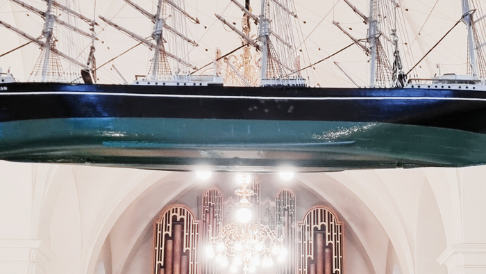 En stor skibsmodell hænger i et belyset og arkitektonisk imponerende rum.