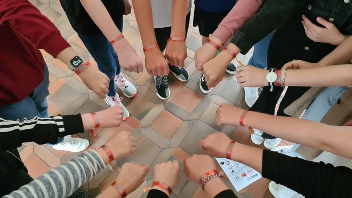 Eine Gruppe von Menschen steht im Kreis und hält ihre Handgelenke mit Armbändern hoch.