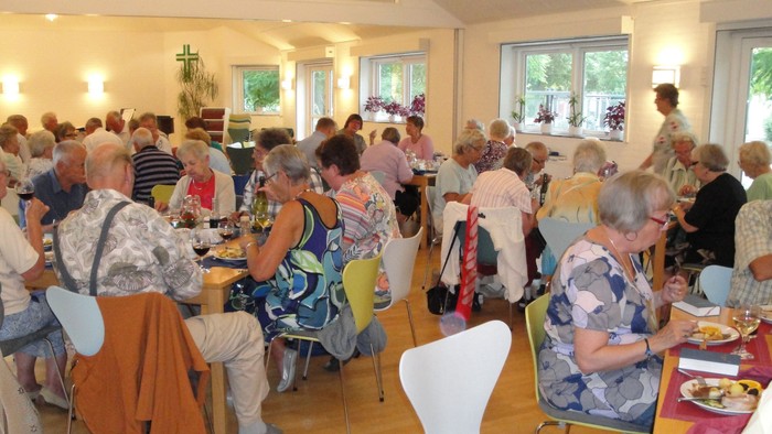 En gruppe ældre mennesker nyder et fælles måltid i en lys, social spisesal.