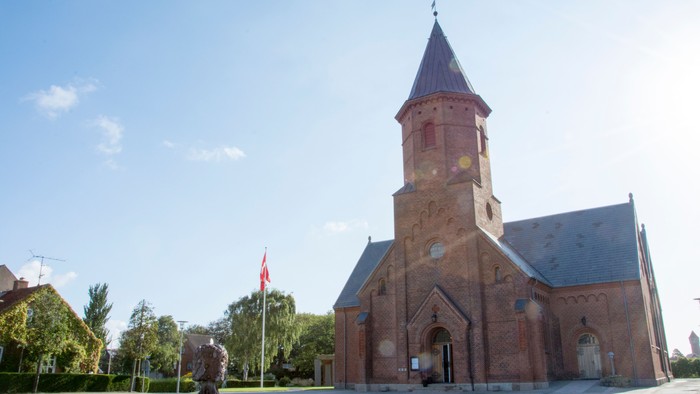 En rød murstenskirke med tårn og en statue foran