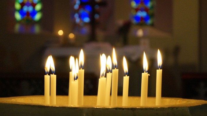 Mehrere brennende Kerzen vor Kirchenfenstern