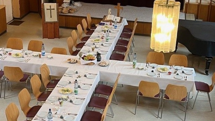 Ein langer Tisch mit Stühlen in einem Raum, der wie eine Kirche aussieht, mit Kerzen und Geschirr gedeckt.