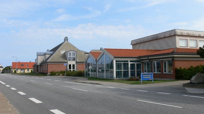 En lang, tom vej med et rødt teglstenshus og et fladt, hvide hus til højre.