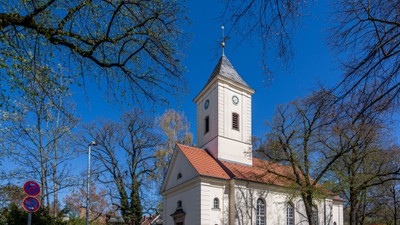 Kleine weiße Kirche mit Uhrturm und rotem Dach unter Bäumen