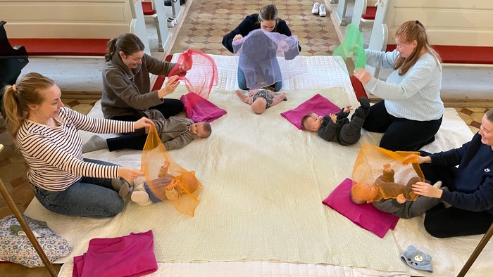 En gruppe af kvinder sidder på gulvmatte og laver håndarbejde.