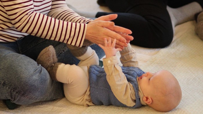 To kvinder leger og hjælper en baby under en siddende gulvaktivitet og smiler varmt sammen.