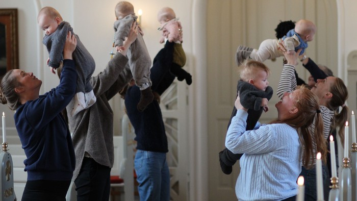 En gruppe voksne holder børn oppe i luften i et rum