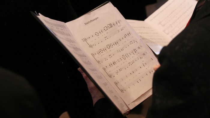 Eine ältere Dame hält ein aufgeschlagenes Liedblatt in der Hand. 