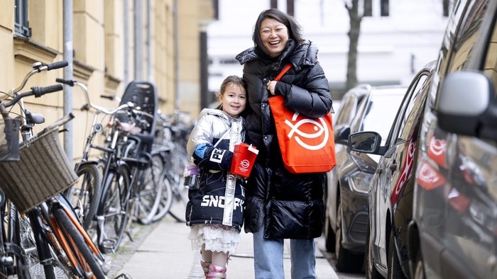 To drenge går med en kvinde på en smal gade med cykler og biler.