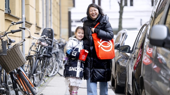 To drenge går med en kvinde på en smal gade med cykler og biler.