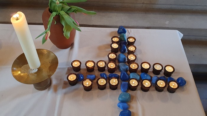 Kerzen, die kreuzförmig auf einem Tisch mit einer Topfpflanze arrangiert sind.