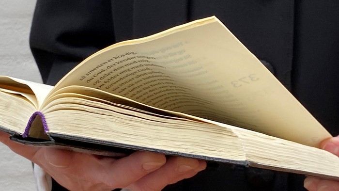 En person holder en åben bog, der er bindet med et violet bånd.