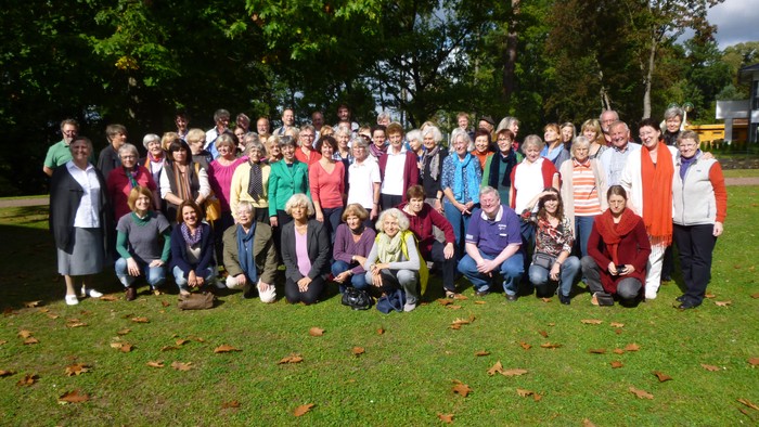 Gruppe von Menschen, die im Freien auf einer grasbewachsenen Fläche mit Bäumen posieren.
