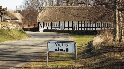 En landsbyvej med skiltet "Vejlby" og huse med strawetage