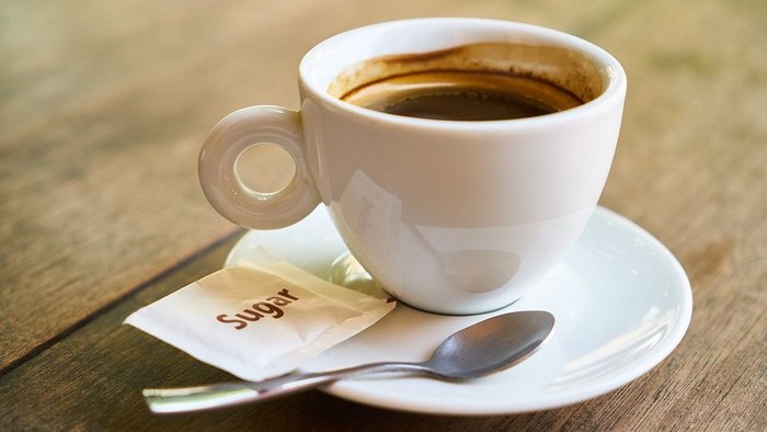 Eine Tasse Kaffee mit Zucker und Löffel auf einem Holztisch.