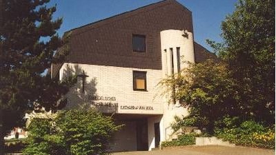 Moderne Kirche mit der Aufschrift „Katharina von Bora Haus“, umgeben von Grünflächen unter klarem blauem Himmel.