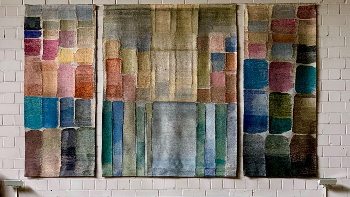 Drei farbenfrohe Wandteppiche hängen an einer weißen Ziegelwand