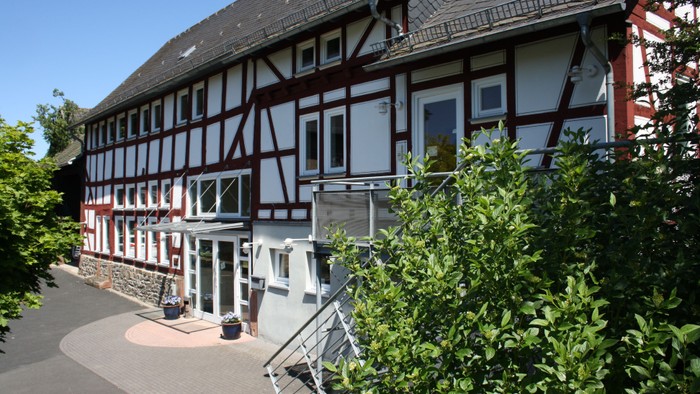 Das Bild zeigt ein traditionelles Fachwerkhaus mit rot-weißer Fassade und einem gepflegten Garten.