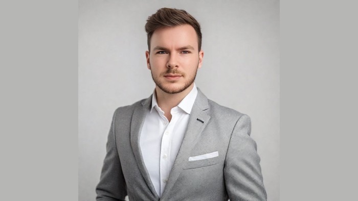 Professionel mand i gråt jakkesæt og hvid skjorte, der poser mod en neutral baggrund.