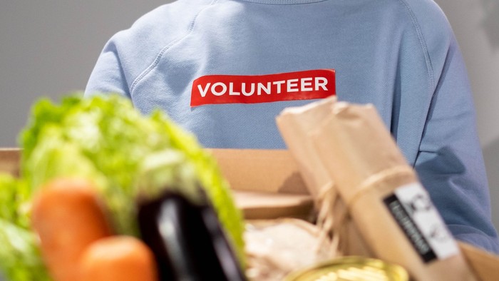 Ein freiwilliger Helfer hält eine Kiste mit Gemüse und Verpackungen