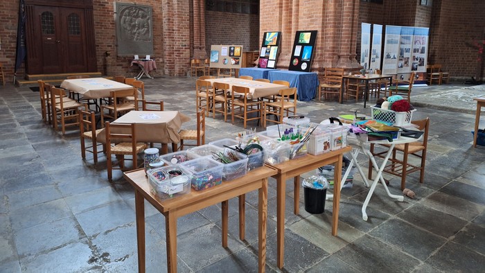 Kunstmaterialer lagt frem på borde i et stort rum med murstensvægger og buer.
