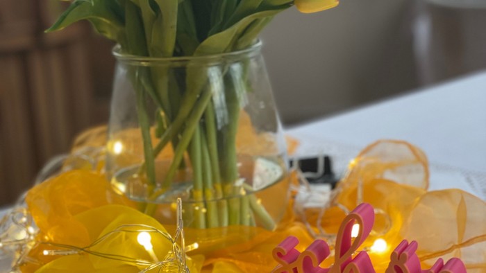 Helle gelbe Tulpen in einer Vase mit Lichterkette und pinkfarbenen Deko-Buchstaben auf einer festlichen Tischdekoration.