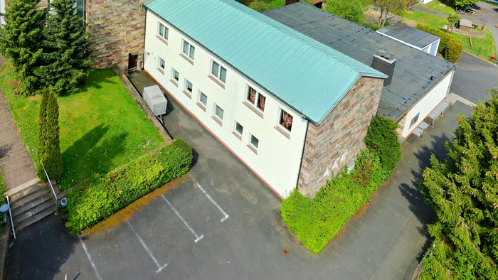 Ein großes Haus mit grünem Dach und gepflegtem Garten, umgeben von Bäumen und anderen Gebäuden.