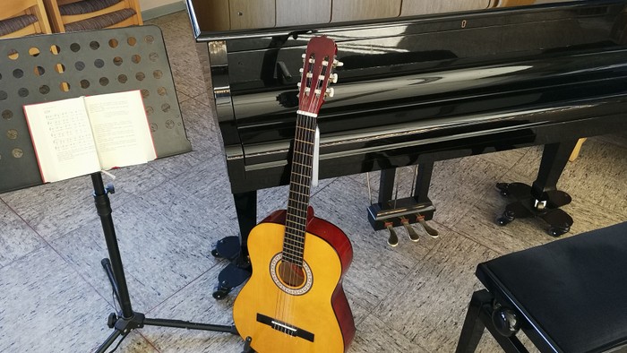 Auf dem Bild sind Gitarre, Notenständer und Klavier zu sehen. 