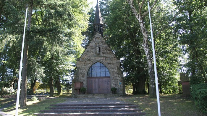Kleine Kirche in Wald mit steinernem Eingang und spitzem Dach.