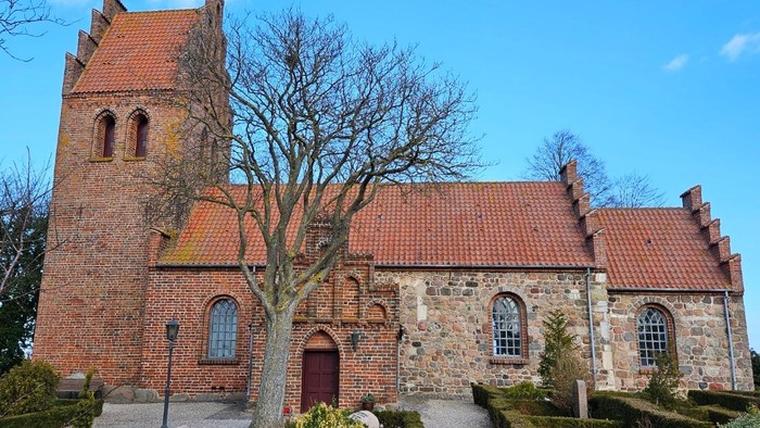 En gammel kirke med røde tag og murstensfasader, omgivet af en smuk have og træer