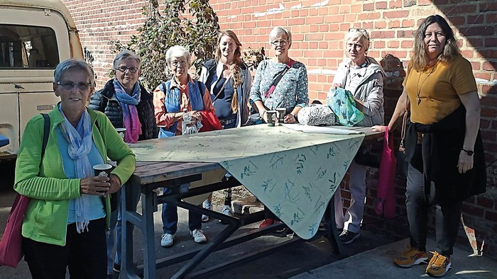 Eine Gruppe von Frauen steht um einen Picknicktisch, eine hält eine Tasse, eine andere ein Telefon.