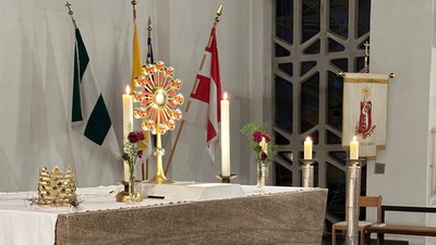Eleganter Kirchenaltar, geschmückt mit Kerzen, Fahnen, Blumengestecken und religiösen Verzierungen auf einem Marmorboden.
