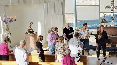 En gruppe samles i en moderne kirke til en gudstjeneste og synger salmer med udsigt til havet udenfor.