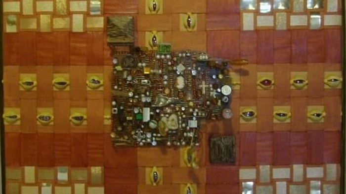 Indviklet mosaikkunst med geometriske mønstre, perler og symbolske øjenmotiver i en træramme.