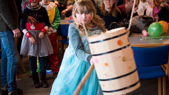 En pige i blå kragekleid og krona spiller med en træstamme og en papirlampe.