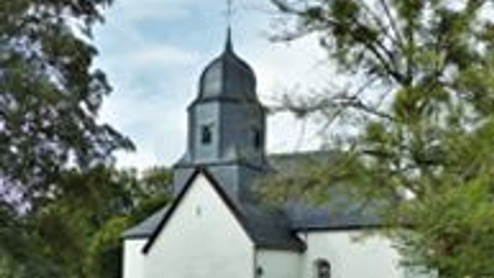 Kleine weiße Kirche mit einem Turm, umgeben von Bäumen.